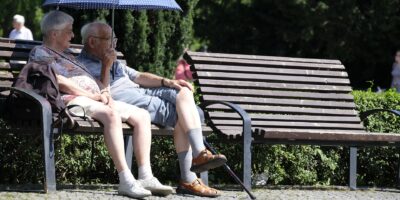 Senioren-Pärchen sitzt mit offenem Sonnenschirm auf einer Bank